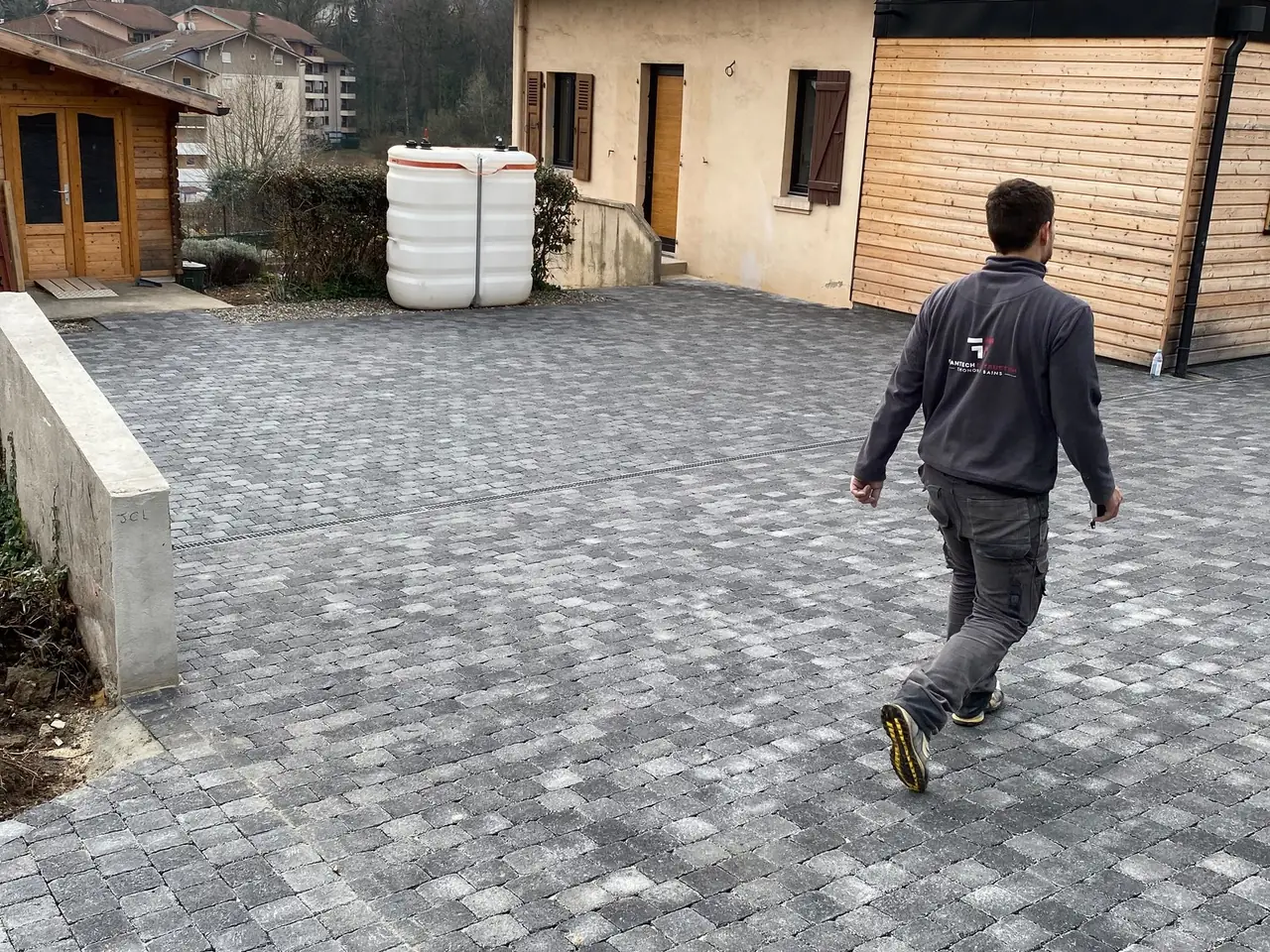 Cour en pavés gris nuancés devant une maison au bardage bois