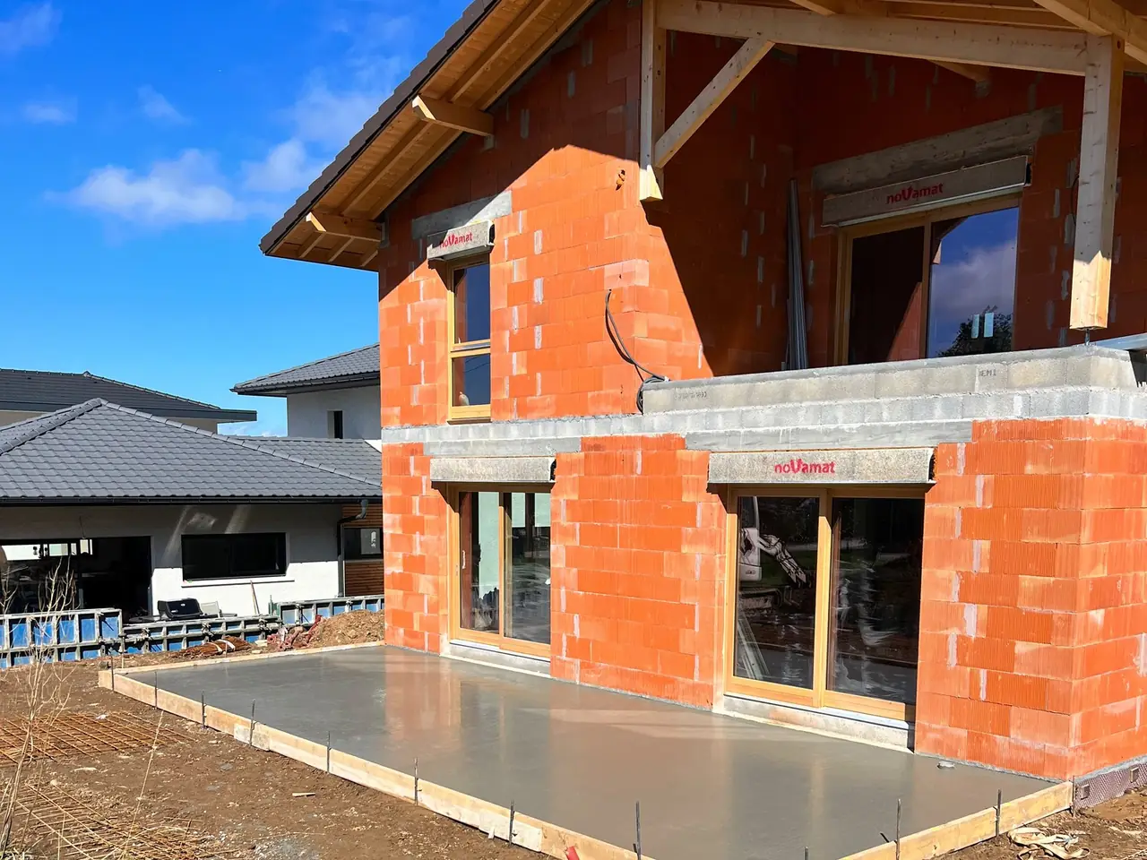 Maison neuve en briques sous sa toiture, dalle de la terrasse coulée devant les baies