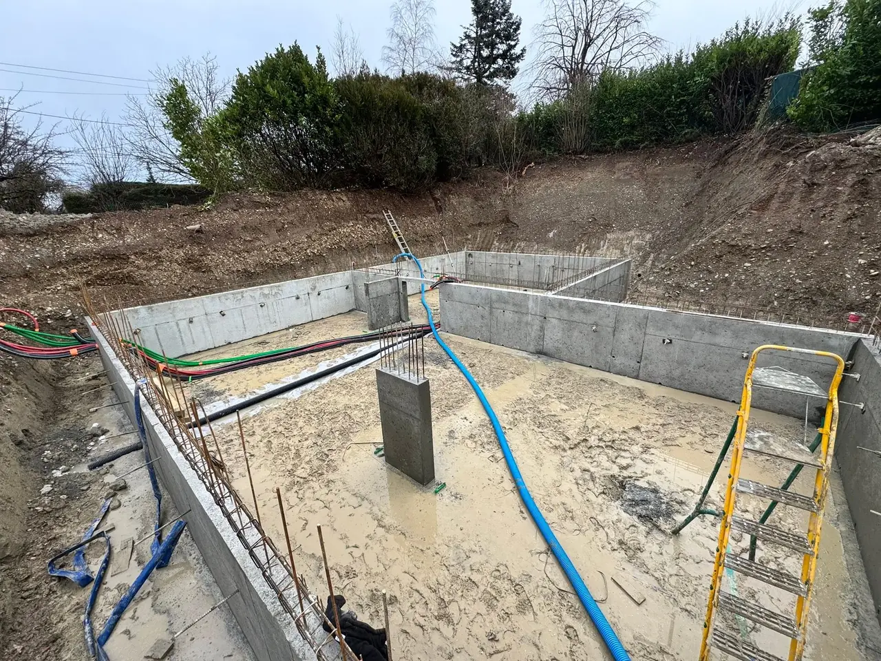 Murs de sous-sol décoffrés et, au centre, un poteau en béton armé dont les aciers attendent le niveau supérieur.