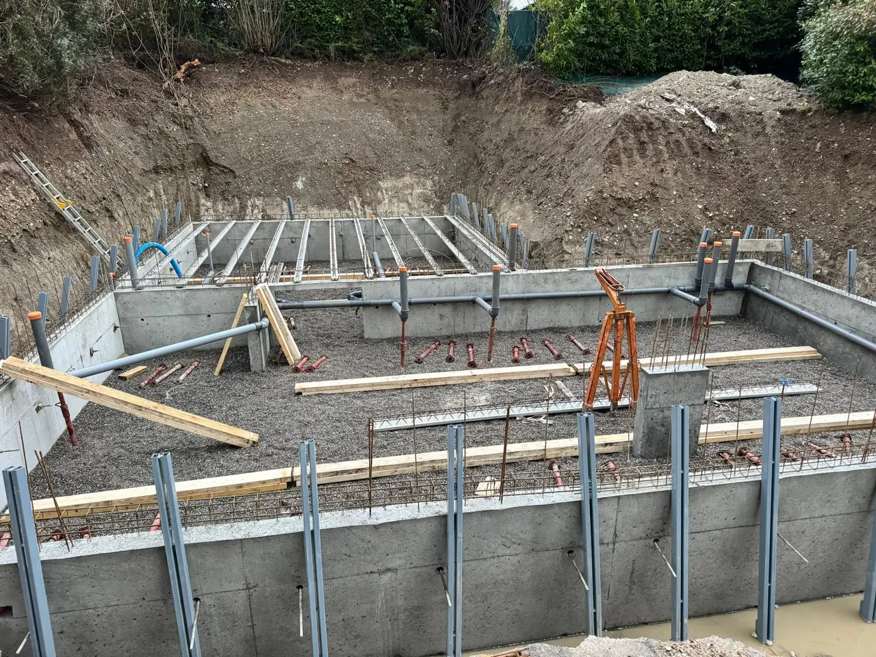 Sous-sol en béton : hérisson de gravier, évacuations en attente, premières poutrelles du plancher posées sur les murs.