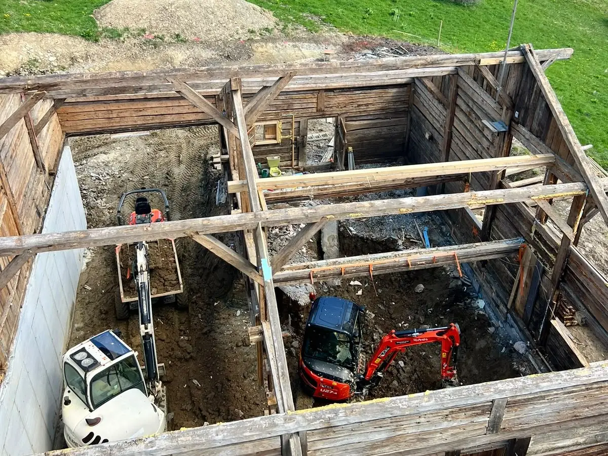 Deux mini-pelles creusent à l’intérieur de la charpente étayée d’un vieux chalet